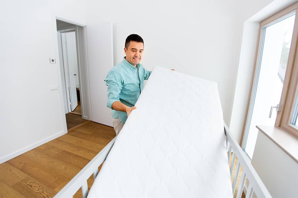 Father placing mattress in baby crib